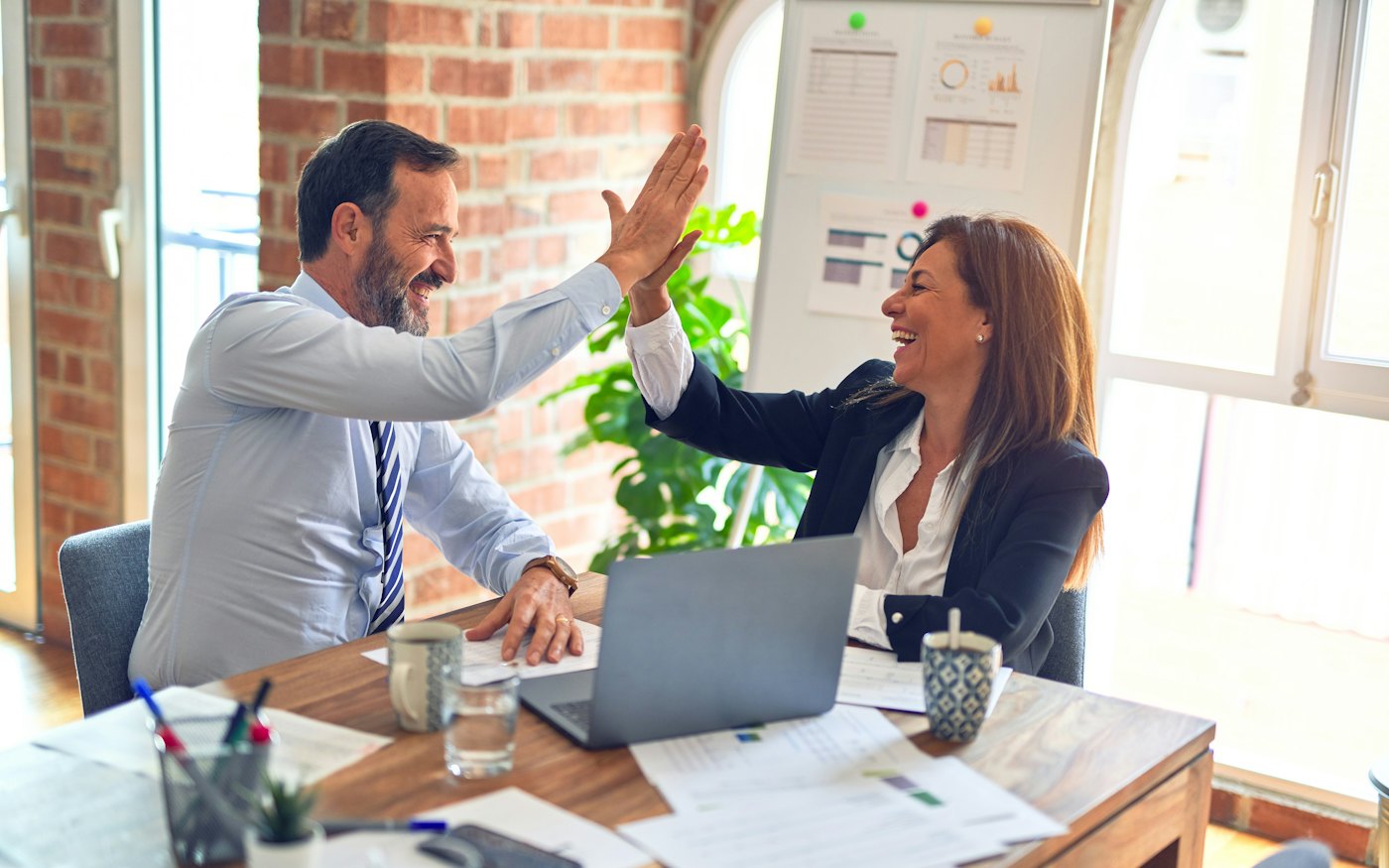 Two colleagues high-fiving over a laptop after a good meeting